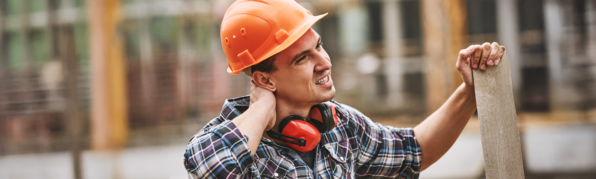 Construction worker in protective helmet feeling neck pain while working at construction site