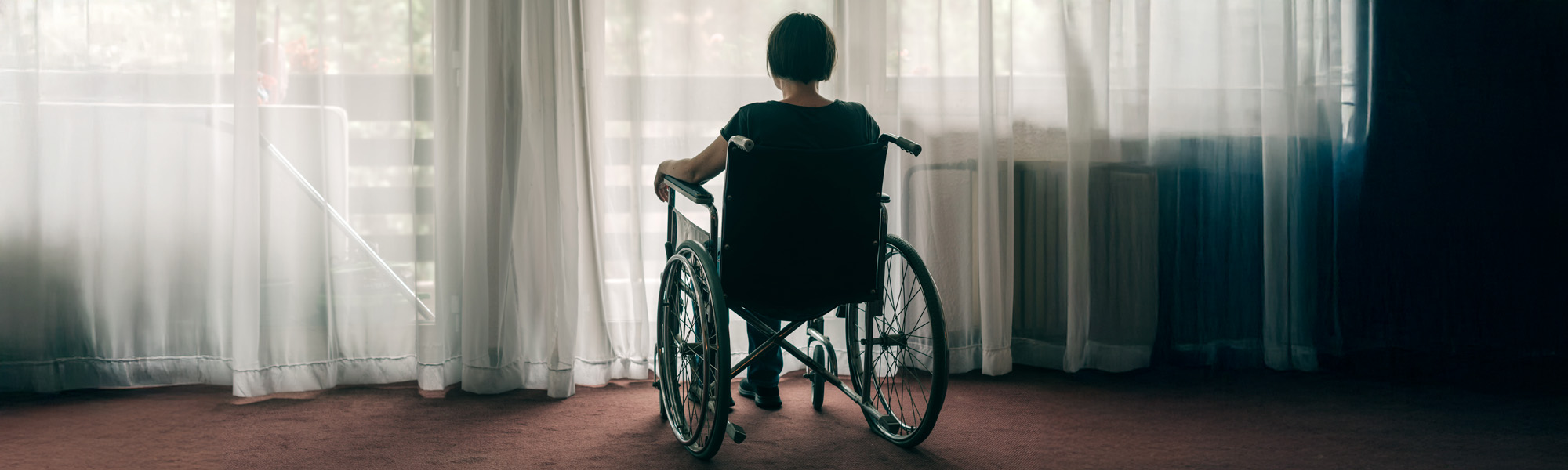 Depressed sad woman in worn wheelchair looking out the window